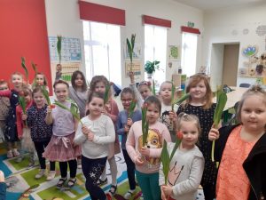 Dziewczynki z oddziału przedszkolnego pozują do zdjęcia z podniesionymi w górę tulipanami.