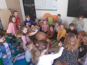 Dzieci siedzą na dywanie w okół Pani opowiadającej o pszczelarstwie.