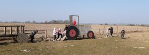 Dzieci bawią się na polu przy drewnianych konstrukcjach wozu i traktora z czerwonymi kołami.