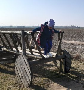 Dziewczynka stoi na przyczepiewykonanej z drewna. Dziewczynka pochyla się do skoku na ziemię.