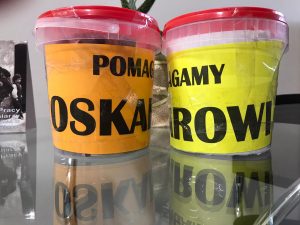 Zdjęcie puszek przygotowanych na zbiórkę pieniędzy. Na pomorańczowym i żóltym tle nadruk POMAGAMY OSKAROWI.