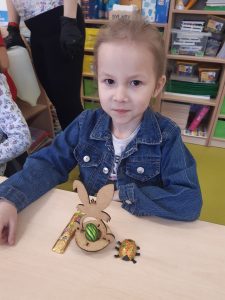 Uczennica siedzi przy stoliku. Przed nią ustawiony jest model zajączka oraz czekoladowy zajączek i żuczek w pazłotku.