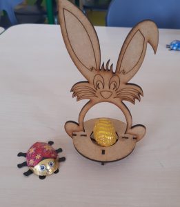 Zdjęcie złożonego modelu zajączka z umieszczonym w podstawie czekoladowym jajeczkiem oraz czekoladową biedronką ustawioną obok modelu.