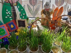 Zdjęcie dekoracji wielkanocnej. Wśród małych doniczek z zieloną trawą ustawiono koszyczki z zajączkami oraz inne wielkanocne dekoracje.