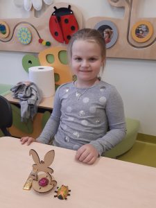 Uczennica siedzi przy stoliku. Przed nią stoi model zajączka z umieszczoną czekoladką po środku.
