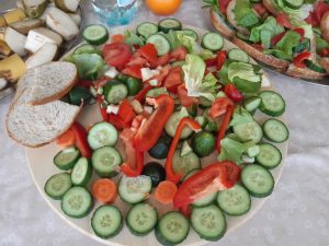 Zdjęcie zdrowego półmiska z ułożonymi takimi warzywami jak: pokrojonymi ogórkami, papryką oraz pociętą sałatą. Na skraju talerza leżą kawałki chleba.