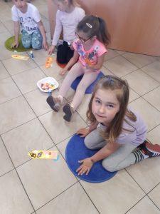 Cztery uczennice oddziału przedszkolnego siedzą na podłodze Biblioteki w Ostaszewie. Przed dziewczynkami leżą wykonane przez nie zakładki orazprzybory, których używały.