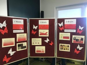 Zdjęcie gazetki stworzonej z okazji majowych świąt. Na każdej z trzech części parawanu umieszczono flagi Polski z nadrukowanymi datami: 1 maja, 3 maja i 2 maja. Pod flagą z data 1 maja napis święto Pracy i zadrukowane trzy kartki z informacjami na jego temat. Pod flagą z datą 2 maja święto flagi i również trzy zadrukowane kartki na temat tego święta. Pod flagą z datą 3 maja również przyczepiono trzy zadrukowane kartki Całość ozdabiają białe i czerwone motyle wycięte z papieru.