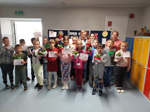 Uczniowie biorący udział w konkursie "Laurka dla mamy lub taty" pozują do grupowego zdjęcia. Dzieci trzymaja w rękach otrzymane dyplomy i upominki.
