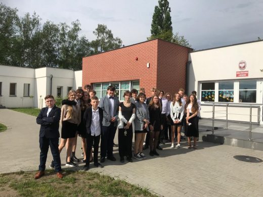 Ósmoklasiści pozują do grupowego zdjęcia przed szkolnym budynkiem.