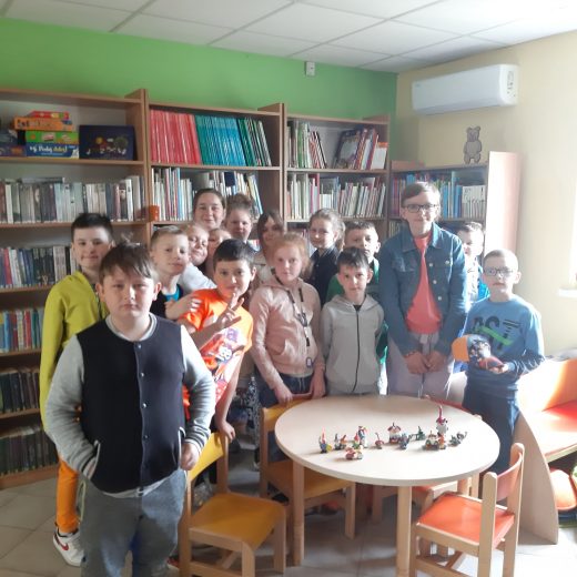 Uczniowie pozują do zdjęcia grupowego w bibliotece w Ostaszewie. Dzieci stoją za stolikiem, na którym ustawione zostały małe figurki.
