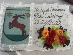 Zdjęcie tortu przygotowanego na galę absolwenta. Obok herbu gminy, napis Najlepsi Absolwenci Roku Szkolnego 2021/2022. Pod napisem pomarańczowej i czerwone róże wykonane z lukru.