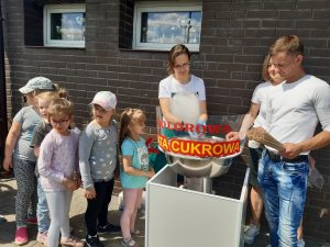 Dzieciz oddziału przedszkolnego stoją w kolejce po watę cukrową. Za maszyną do robienia waty stoi obsluga.
