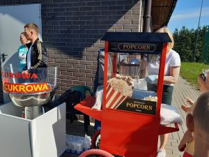 Zdjęcie maszyny do popcornu i waty cukrowej ustawionych na szkolnym orilku. Za maszynami stoją obslugujący je pracownicy.