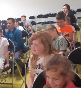 Zbliżenie na uczniów ogladających przedstawienie. Dzieci siedzą na krzesełkachustawionych na sali teatralnej.