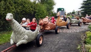 Zdjęcie kolejki z wagonikami przypominającymi dinozaury.W wagonikach siedzą uczniowie oddziału przedszkolnego.