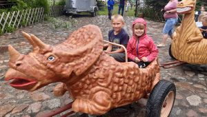 Dwoje uczniów oddziału przedszkolnego siedzi w wagoniku przypominającym dinozaura. Dzieci się usmiechają.