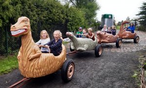 Zdjęcie kolejki z wagonikami przypominającymi dinozaury.W wagonikach siedzą uczniowie oddziału przedszkolnego.