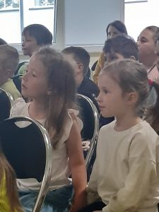 Zbliżenie na uczniów ogladających przedstawienie. Dzieci siedzą na krzesełkachustawionych na sali teatralnej.