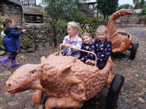 Trzy dziewczynki z oddziału przedszkolnego siedzą w wagoniku przypominającego dinozaura. Za nimi ustawiony jest kolejny pusty wagonik.