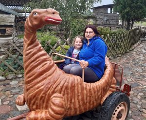 Uczennica siedzi z Panią w wagoniku przypominającym dinozaura.