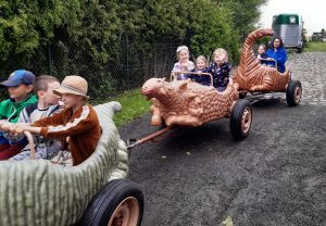 Zdjęcie kolejki z wagonikami przypominającymi dinozaury.W wagonikach siedzą uczniowie oddziału przedszkolnego.
