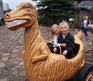 Dwie uczennice oddzialu przedszkolnego przytulają się siedząc w wagoniku przypominającym dinozaura.