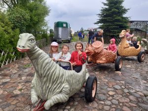 Dzieci z oddziału przedszkolnego siedzą w połączonych wagonikach przypominających dinozaury.