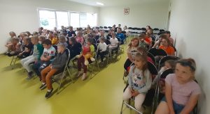 Uczniowie siedzą na krzesłach na sali teatralnej i oglądają przedstawienie.