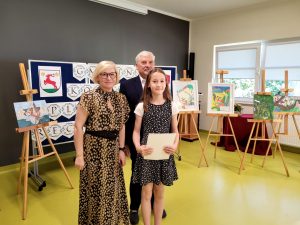 Pani Dyrektor i wójt pozują do zdjęcia z jedną z nagrodzonych uczennic. Dziewczynka trzyma w ręku dyplom.