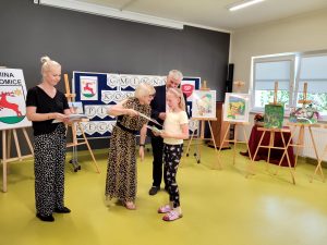 Pani Dyrektor wraz z Panem Wójtem wręczają uczennicy dyplom i nagrodę książkową za udział w gminnym konkursie plastyczno - recytatorskim. Obok stoi nauczycielka - jedna z organizatorek konkursu.