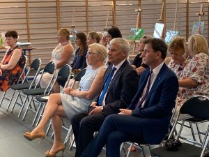 Zdjęcie zaproszonych na zakończenie roku szkolnego gości - Pani Sekretarz, Wójta Gminy Łysomice oraz Inspektora ds. Oświaty. Goście siedzą na honorowych miejscach w pierwszym rzędzie a za nimi nauczyciele zkoły Podstawowej w Ostaszewie.