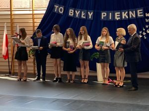 Najlepsi absolwenci naszej szkoły stoją w jednym rzędzie. Obok nich Pani Dyrektor z wójtem oraz dwoje uczniów prowadzących galę.
