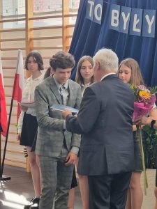 Wójt Gminy Łysomice ręcza świadectwo uczniowi, który uzyskał świafevtwo z wyróżnieniem. W tle stoją pozostali wyróżnieni ósmoklasiści.