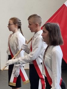 Zdjęcie nowego pocztu flagowego. Uczniowie mają przełożone biało-czerwone szarfy a uczeń stojący po środku trzyma flagę Polski.