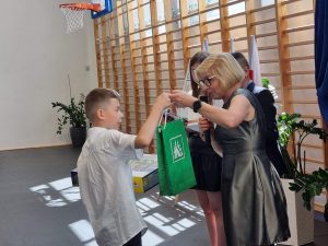 Uczeń podczas odbierania nagrody od Pani Dyrektor, która przekazuje mu zieloną papierową torbę.