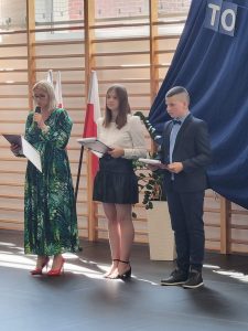 Przedstawicielka rodziców klasy ósmej podczas przemówienia. Obokniej stoją uczniowie prowadzący galę zakończenia roku.
