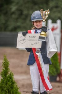 Uczennica Maja Iwińska prezentuje otrzymane nagrody - w jednej dłoni trzyma puchar, zaś w drugiej voucher.