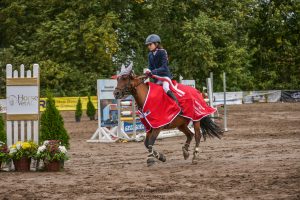 Uczennica Maja Iwińska siedzi na koniu w galopie. W tle widac ustawione przeszkody.