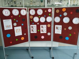 Zdjęcie gazetki przygotowanej z okazji dnia kropki. Na mobilnej tablicy umieszczono napis DZIEŃ KROPKI - każda litera została wydrukowana w osobnym kółeczku. Pod spodem umieszczono kolorowe kropki oraz karty z informacjami na temat dnia kropki.