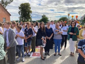 Uczniowie wraz z rodzicami stoją na szkolnym boisku podczas inaguracji roku szkolnego 2022/2023.