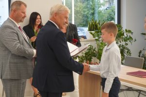 Uczeń Tomasz Masny przyjmuje gratulacje od wójta Gminy Łysomice. Wójt w jednej ręce trzyma dyplom a drugą podaje uczniowie. Obok wójta stoi przewodniczący Rady Gminy.