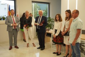 W półokręgu stoją przedstawiciele gminy, uczennica Weronika Zielińska i jej rodzice. Stojący po środku wójt gminy trzyma dyplom dla uczennicy.