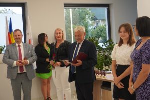 Wójt Gminy Łysomice patrzy na trzymany w rękach dyplom. Obok wójta po lewej stronie stoją przedstawiciele gminy, zaś po prawej uczennica Zuzanna Owczarczyk z mamą.