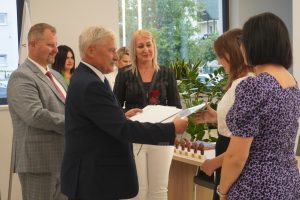 Uczennica Zuzanna Owczarczyk otrzymuje od wójta Gminy Łysomice dyplom za osiągnięcia w nauce. Obok uczennicy stoi jej mama a za wójtem przedstawiciele gminy.