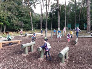 Uczniowie podczas zabawy na placu przy szkole leśnej na Barbarce. Dzieci z pierwszego planu bawią się przy ustawionych w rzędzie drewnianych koziolkach.