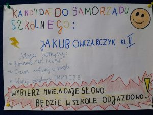 Zdjęcie plakatu kandydata do małego Samorządu Uczniowskiego. Na białym tle kolorowy napis: :KANDYDAT DO SAMORZĄDU SZKOLNEGO: JAKUB OWCZARCZYK KL II Mojepomysły: -Konkurs MAM TALENT, - Dzień pizamy w szkole - Więcej szkolnych IMPREZ ! WYBIERZ MNIE, ADAJE SLOWO BĘDZIE W SZKOLE ODJAZDOWO!" Plakat ozdobiony rysunkiem usmiechniętego słońca i piorunem.