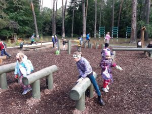 Uczniowie podczas zabawy na placu przy szkole leśnej na Barbarce. Dzieci z pierwszego planu bawią się przy ustawionych w rzędzie drewnianych koziolkach.