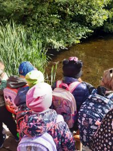 Uczniowie oddziału przedszkolnego stoją przy stawie i patrzą na wodę.