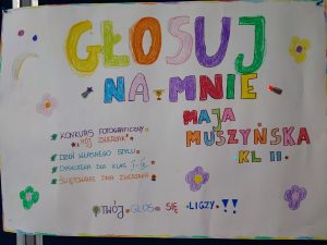 Zdjęcie plakatu kandydatki do małego Samorządu Uczniowskiego. Na białym tle kolorowe napisy: "GŁOSUJ NA MNIE MAJA MUSZYŃSKA KL II - KONKURS FOTOGRAFICZNY, - DZIEŃ WSŁASNEGO STYLU, - DYSKOTEKA DLA KLAS I-III, - ŚWIĘTOWANIE DNIA ZWIERZĄT; TWÓJ GŁOS SIĘ LICZY !!". Plakat ozodbiono kolorowymi kwiatkami.